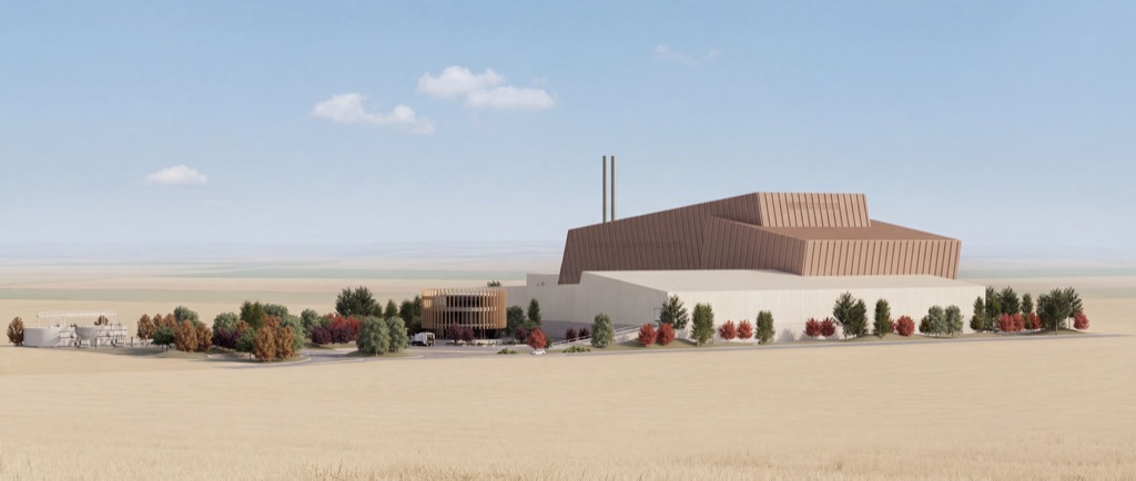 Vista general del conjunto: a la izquierda, instalaciones auxiliares y un edificio circular de lamas de madera; en el centro y a la derecha, la nave de hormigón claro y el volumen de cobre con sus dos chimeneas, entre arbolado y campos de cereal.